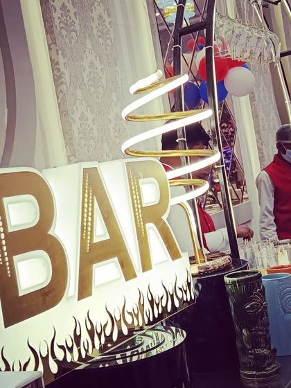 A close-up of our light-up 'BAR' sign with a flame motif, paired with tiki glasses and modern spiral lighting.