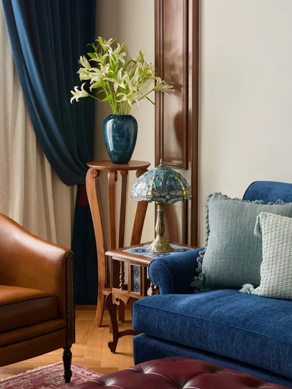 A closer look at the details in this Maddock lounge reveals the intentional layering of textures and light. A vintage Tiffany lamp casts a soft glow on the rich blue sofa and tan leather armchair, creating a warm and inviting corner perfect for collaboration and creative discussions.