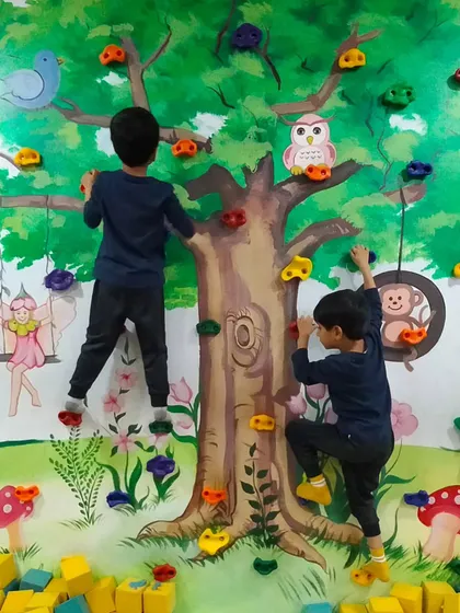 The climbing wall is a fantastic tool for building upper body strength and coordination. Here you can see two boys working their way up the tree themed wall, surrounded by a soft foam pit for safety.