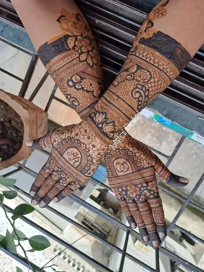 A full view of an engagement mehndi, with initials and rings, set against a background of lush greenery.
