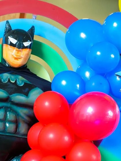 Batman stands ready to welcome guests, surrounded by colorful balloons and comic-style "ZAP!" signs.
