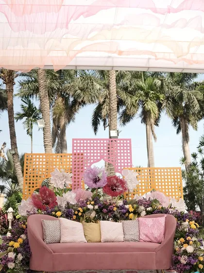 A chic seating area for a pastel carnival event. The dusty rose sofa is set against a backdrop of colorful lattice screens and oversized paper flowers, with soft, ruffled drapes overhead.