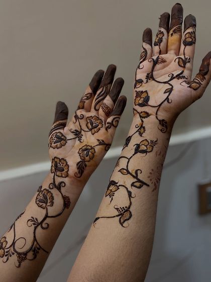 A full view of a gorgeous Gulf henna design with flowing vines and flowers covering both hands and arms.