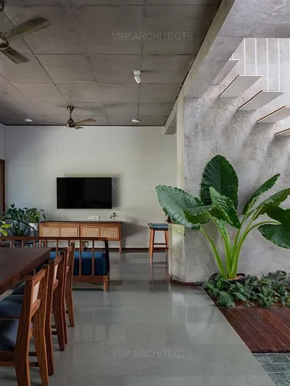 Inside 'HAVEN', an open-plan living and dining area features a raw concrete ceiling and a striking floating staircase, with indoor plants blurring the line between inside and out.