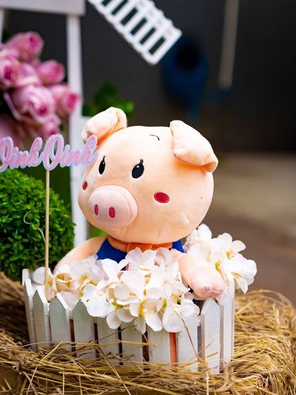 It's all in the details. A cute plush piglet sits in a white picket fence planter, adding a touch of sweetness and charm to the overall barnyard theme decor.