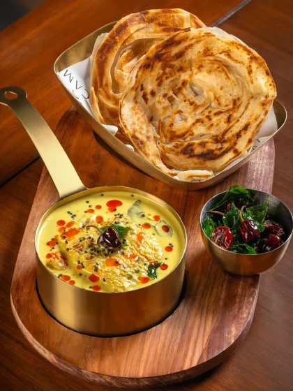 A creamy South Indian style curry served with flaky Malabar parottas for Camo Noida. The vibrant yellow color and tempering on top look delicious.