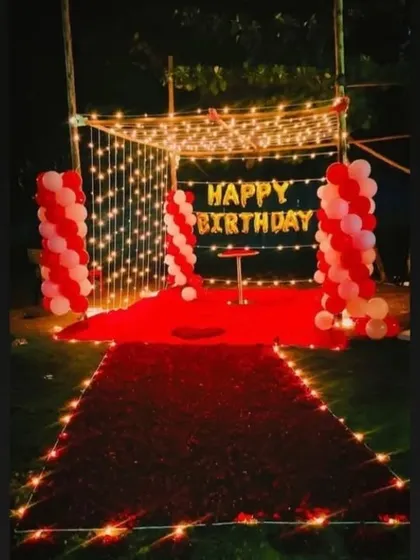 An enchanting outdoor birthday dinner setup. A canopy of fairy lights, a red carpet of rose petals, and balloon columns create a truly magical and romantic experience.