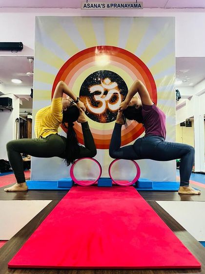 Partner work helps in achieving deeper expressions of a pose. Here, students practice a variation of Kapotasana (Pigeon Pose) using yoga wheels for support.