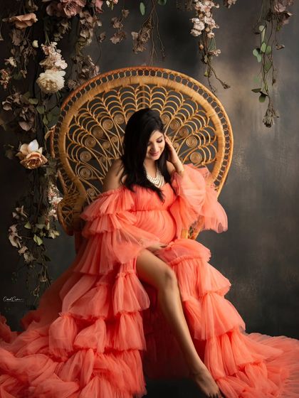 A quiet, regal moment captured in my studio. The mom-to-be is seated on the peacock chair, draped in a stunning orange gown, surrounded by a rustic floral arrangement.