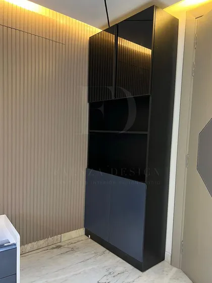 A tall, modern storage cabinet in a bedroom. The design combines open shelving with fluted glass and solid doors, offering a mix of display and concealed storage options.