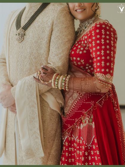 A close-up focusing on the couple's embrace, with the bride's vibrant red lehenga contrasting beautifully with the groom's ivory sherwani. It's a shot that highlights connection and detail.