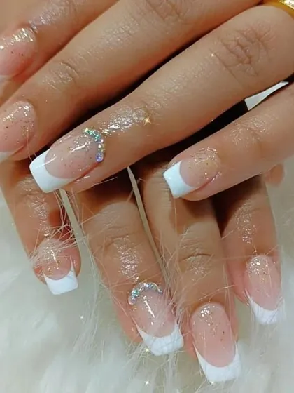 A full view of the classic French manicure with a glitter base and rhinestone accents on the ring fingers.