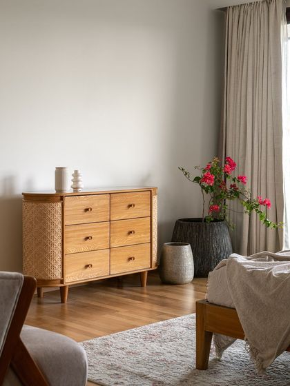 A custom wooden dresser with woven side panels provides stylish storage in this serene bedroom, complemented by rustic planters.
