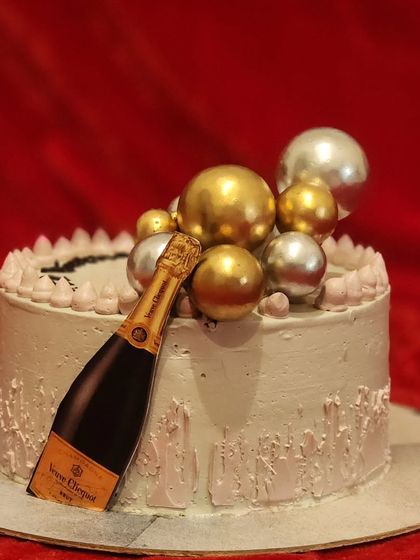 A sophisticated celebration cake perfect for milestone birthdays or anniversaries. This chocolate cake is decorated with a champagne bottle cutout and a cascade of gold and silver decorative spheres.