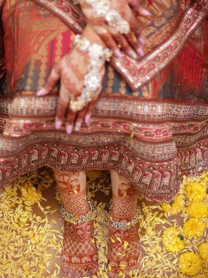 The bride's feet, adorned with intricate stained henna and anklets, resting on a bed of yellow flowers.