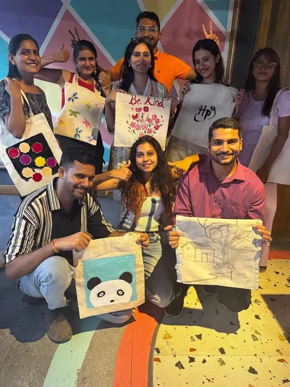 A group of friends having a blast and showing off their newly painted tote bags, featuring everything from a panda to abstract designs.