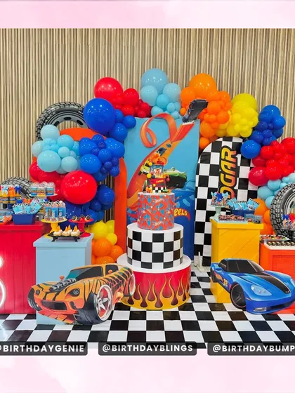 This Hot Wheels themed party is a dream for any young racing fan, featuring a complete dessert station with themed plinths and a custom cake. The backdrop includes a checkered floor mat, race car cutouts, and vibrant balloon decorations to create a high-energy race track environment.