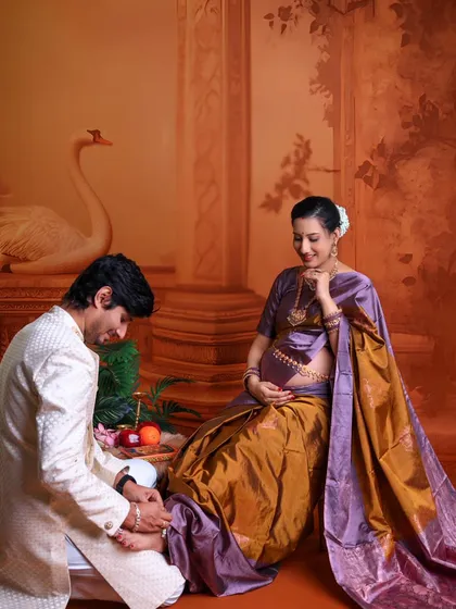 This shot captures a beautiful, traditional gesture of love and care. The husband-to-be attends to his wife's feet as she sits, adorned in a stunning silk saree.