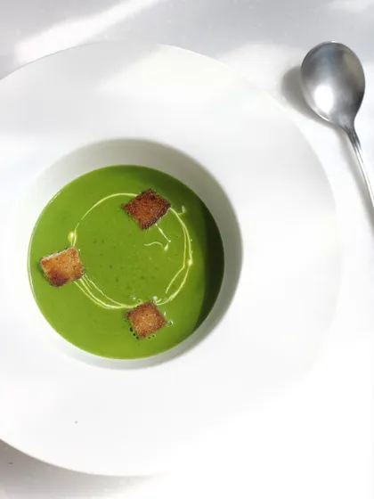 A vibrant green pea soup with croutons. We teach the fundamentals of soup making, from purées and bisques to clear consommés.