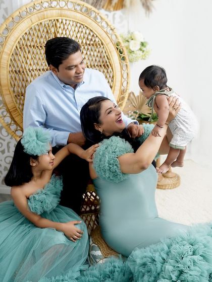 A playful and candid family moment. The mother lifts her baby boy while the father and sister look on with love and laughter.