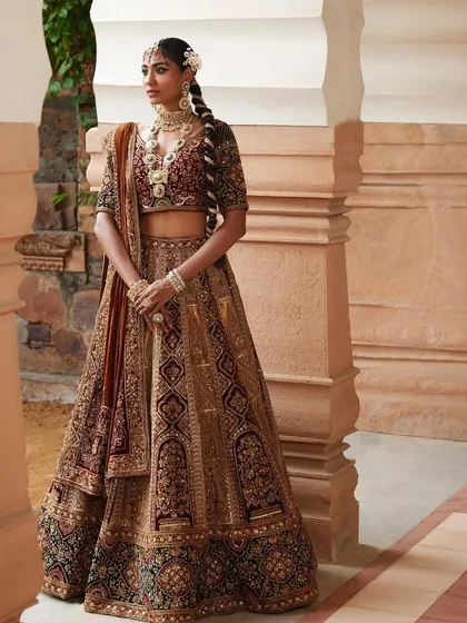 A full-length bridal look from a Wedding Asia campaign, featuring a heavily embroidered velvet lehenga. The styling, including the braided hair with floral details, was designed to create a look of traditional grandeur and opulence.