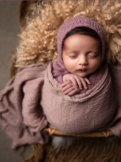 Another angle of the baby wrapped in purple, nestled in a basket on a bed of soft wool.