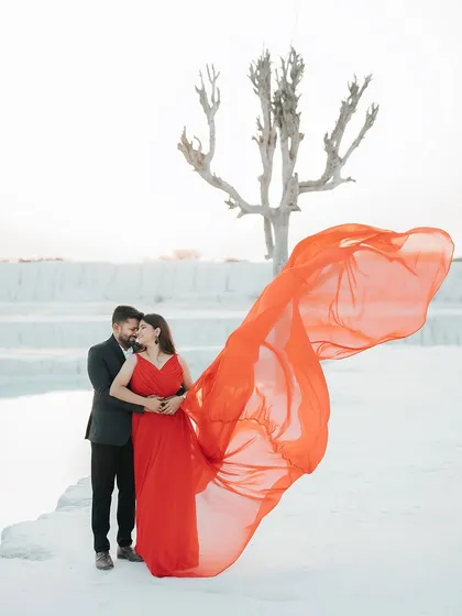 A bold and dramatic shot from a pre-wedding session at a mineral quarry. The vibrant red of the flowing gown against the stark white landscape creates a powerful, high-fashion image that tells a story of passionate love.