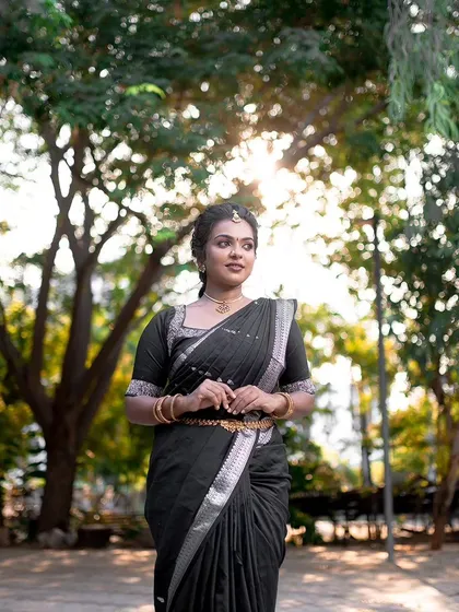 A full-length outdoor shot of the model in a black saree. Her posture is elegant, and her makeup looks fresh and natural in the daylight.