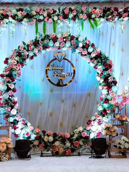 A beautiful floral ring stage for an engagement. The ring is adorned with pink and white flowers, set against a backdrop of white drapes and warm lights.