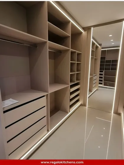 A long, galley-style closet with open shelving and drawers. The integrated strip lighting along the floor and ceiling ensures the entire space is well-lit and easy to navigate.