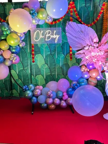If you prefer a modern aesthetic, I design vibrant balloon-based decorations. This setup features a circular ring with multi-colored chrome balloons, a stylish 'Oh Baby' neon sign, and a tropical banana leaf backdrop for a fresh and trendy baby shower.