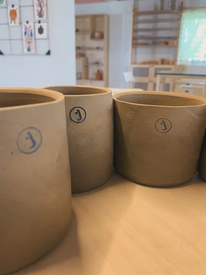 A row of student-made pots, each stamped with our 'J' logo. A proud moment for every new potter.