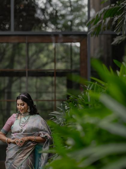 A candid moment of the model adjusting her saree, the soft light filtering through the leaves creating a beautiful effect.