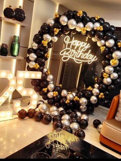 A classy 25th birthday celebration with a black and silver balloon ring. The large marquee numbers and neon sign make it a perfect setup for an adult party.