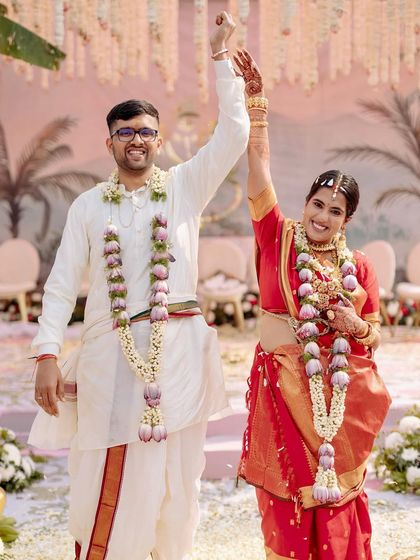 A joyous couple celebrates their South Indian wedding. The decor features traditional elements like lotus garlands and a color palette of red and white, creating an authentic and beautiful ceremony.