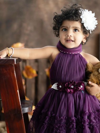 Toddlers are born to make people smile. This little girl in her beautiful purple dress is holding her favorite teddy, which helps make her feel comfortable.