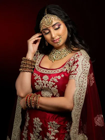 A classic red lehenga look for a North Indian bride. The makeup is kept timeless with gold tones on the eyes and a warm red lip, complemented by a traditional maang tikka and nath.