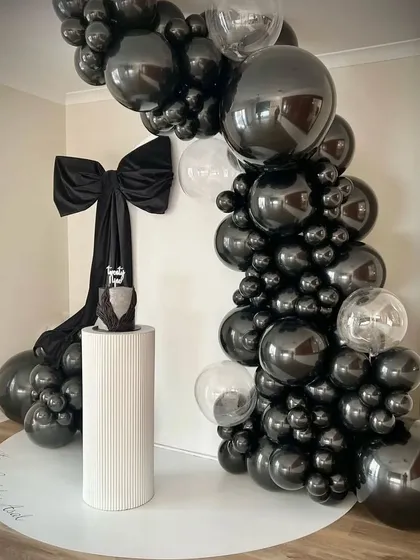 The complete setup for the stylish 29th birthday, with the cake on a pedestal in front of the dramatic black balloon arch.