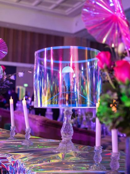 A unique table centerpiece featuring an iridescent lampshade and vibrant pink florals. Even the smallest details are designed to align with the overall theme of modern glamour.