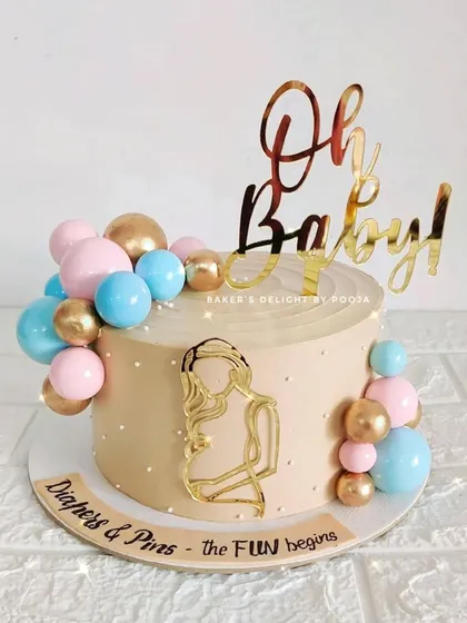 "Diapers & Pins, the fun begins." This baby shower cake uses a lovely beige base with pink, blue, and gold balloon clusters to celebrate the new arrival. The acrylic mom-to-be silhouette adds a personal touch.