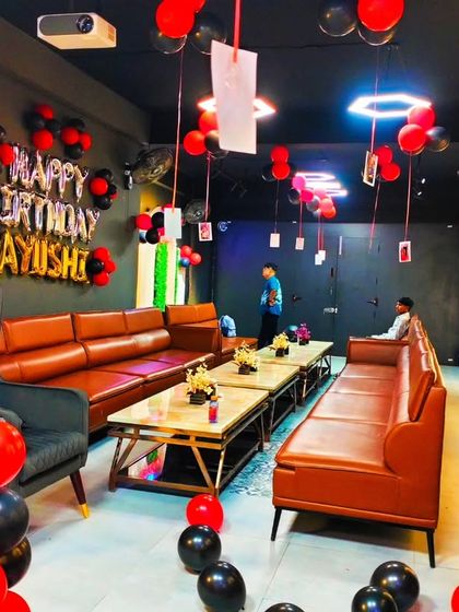 A full view of the red and black themed party in a private room, showing the "Happy Birthday" banner and balloons scattered around.