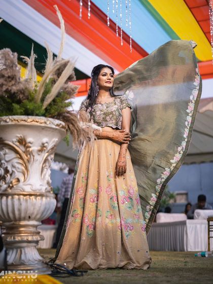 The bride, Disha, looking stunning with her dupatta flowing in the wind. Her makeup is fresh and radiant, perfect for an outdoor wedding event.
