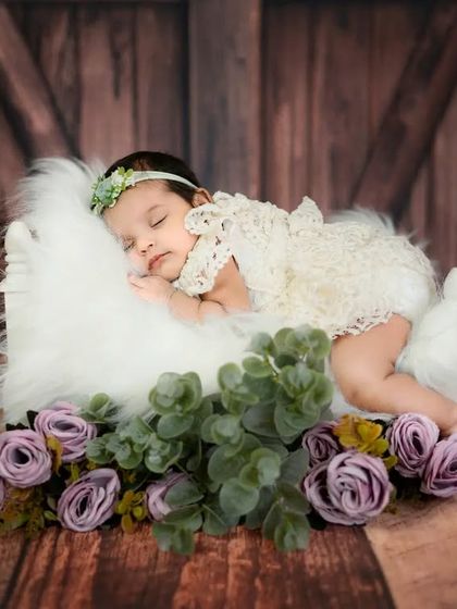 A beautiful newborn girl sleeping on a tiny bed made of feathers. The rustic wooden backdrop adds a warm and charming touch to this portrait.