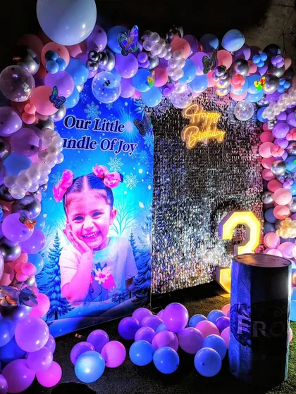 A magical 'Frozen' themed birthday party. The setup includes a custom photo backdrop, a shimmering curtain, a pastel balloon arch, and a light-up number '3'.