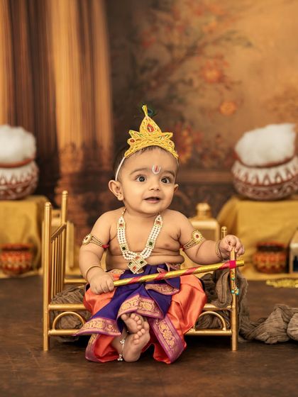 This little Krishna is ready for his close-up! His big, curious eyes and adorable costume make for an unforgettable portrait on his miniature golden bed.