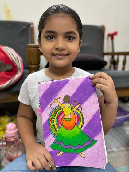 A student holds her beautiful drawing of a garba dancer, capturing the movement and vibrant colours of Navratri.