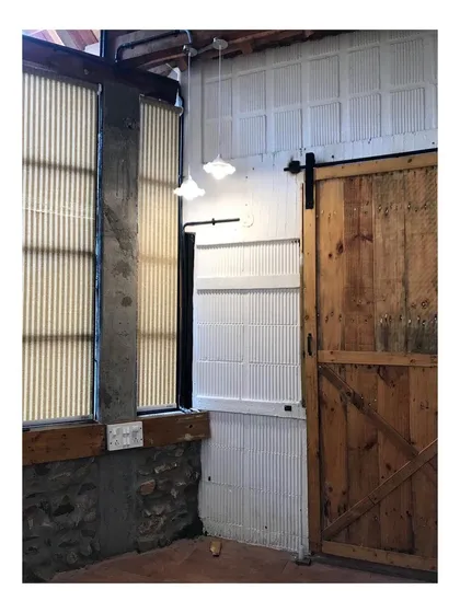 This corner of a farmhouse shows my principle of using honest materials. A rustic sliding barn door made of natural wood is set against a wall of exposed stone and concrete, creating a raw, textural, and authentic feel.