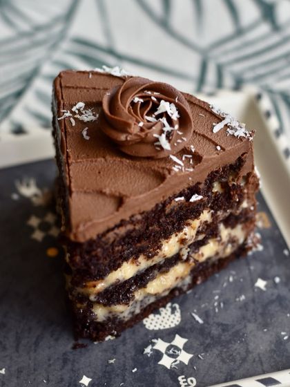 Dee's German Chocolate Cake is a rich and indulgent slice of heaven. It has layers of dark chocolate cake, a fudgy coconut filling, and caramelised walnuts, all covered in a 54% chocolate ganache.