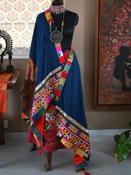 The shawl draped to reveal its dynamic, asymmetrical design. The colorful patchwork trim adds a playful contrast to the earthy tones of the Kalamkari and the deep blue of the cotton.