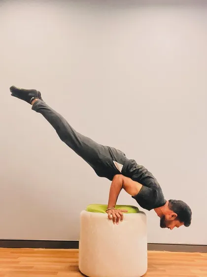 Peacock Pose (Mayurasana) on an ottoman. Using a prop like this can help in learning the alignment for this very challenging arm balance.